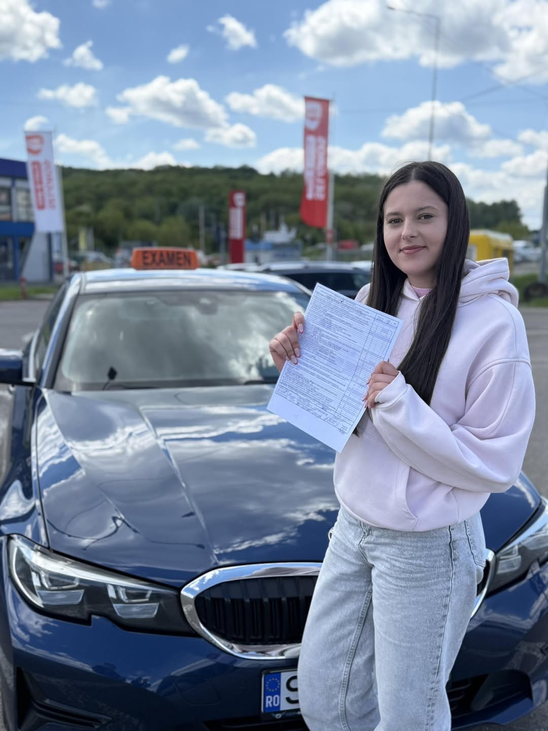 Absolventă AutoStar Drive cu documentele de examen, lângă mașina de școală